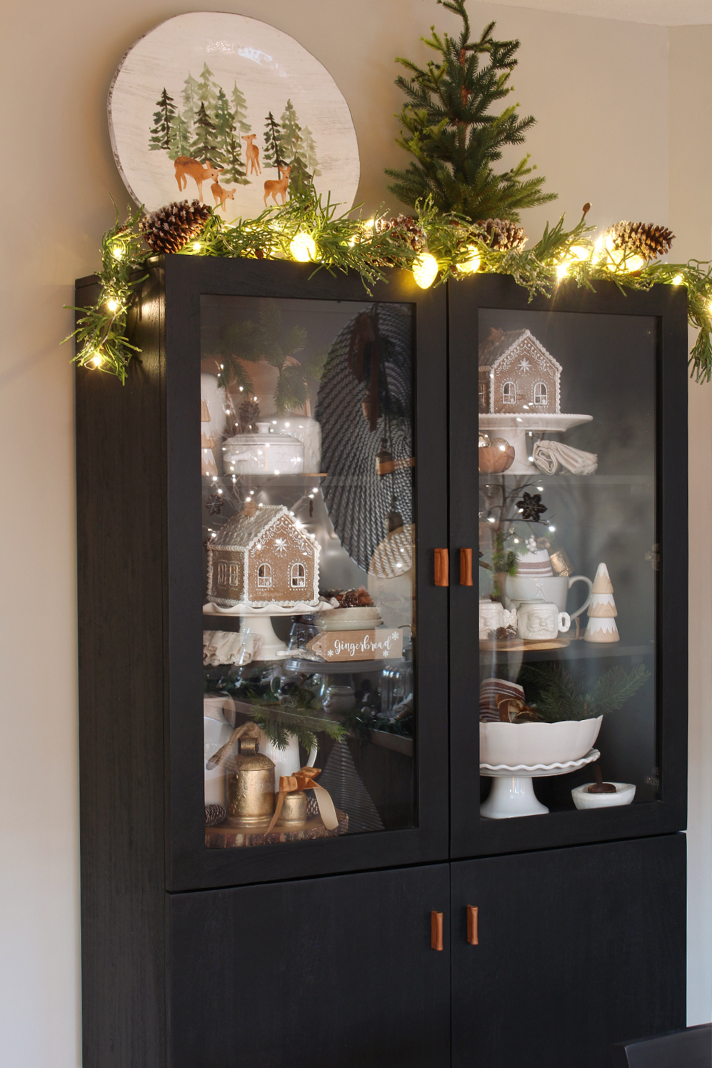 Black dining room cabinet decorated for Christmas with garland, lights and gingerbread houses.