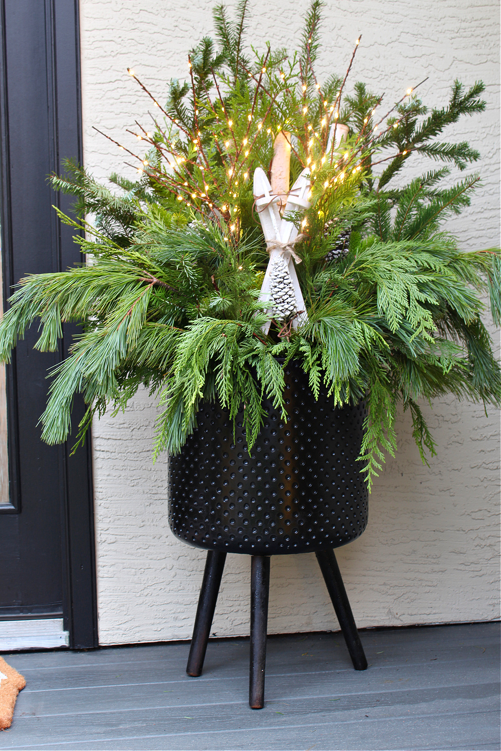Christmas planter with fresh greenery and lighted branches.