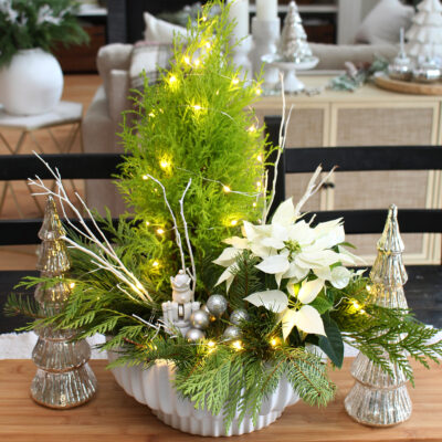 Fresh greenery Christmas centerpiece using a lemon cypress and poinsettia. Embellished with twinkle lights and a nutcracker. #Christmascenterpiece #centerpieceideas #Christmasdecor #Christmascrafts #ChristmasDIY