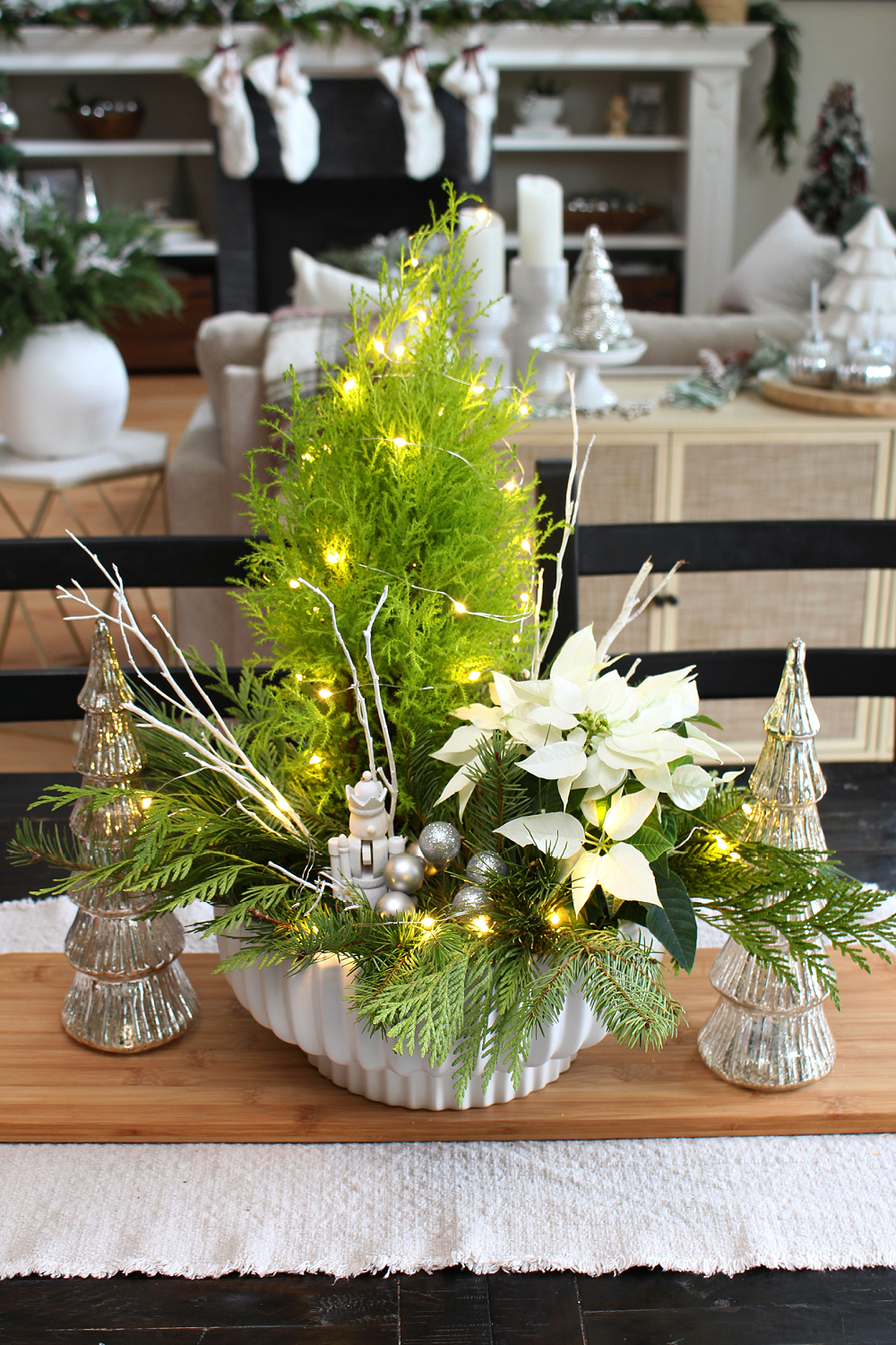 Fresh greenery Christmas centerpiece using a lemon cypress and poinsettia. Embellished with twinkle lights and a nutcracker. #Christmascenterpiece #centerpieceideas #Christmasdecor #Christmascrafts #ChristmasDIY