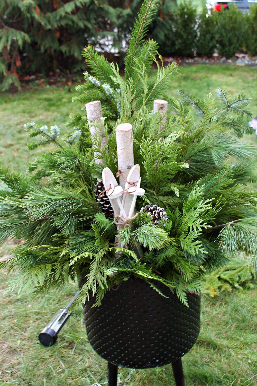 Outdoor Christmas planter with fresh greenery, wood skis, and pine cones.