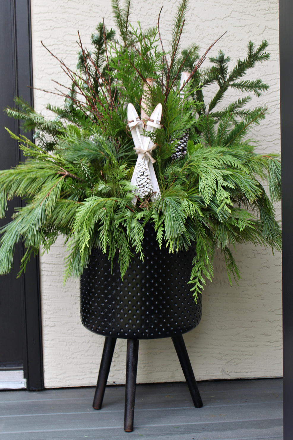 Christmas planter with fresh greenery and wood skis in a black planter.