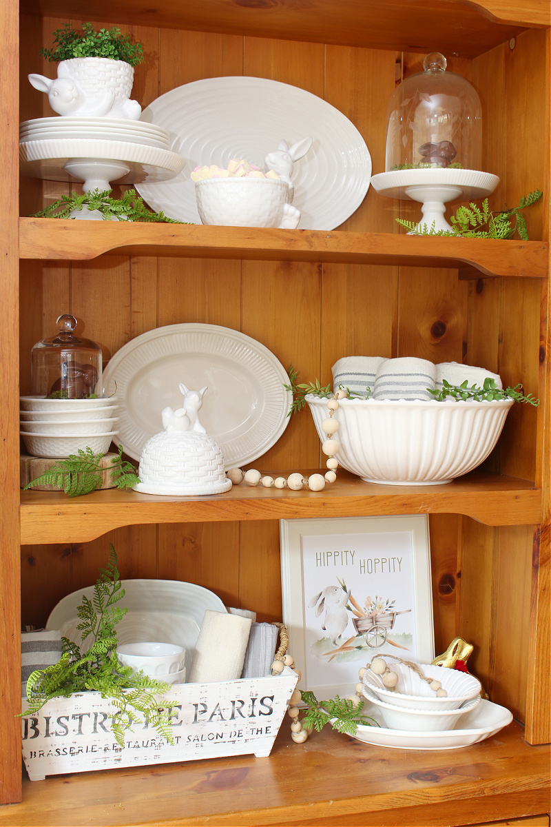 Wood hutch decorated for Easter with white dishware and white bunnies.