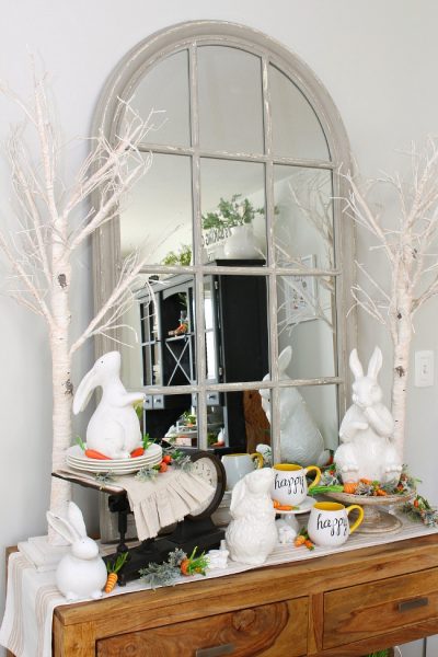 Dining room sideboard decorated for spring with white ceramic bunnies and twinkle light trees.