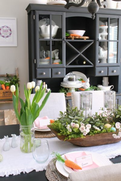 Easter tablescape with dough bowl centerpiece, tulip, and black hutch.