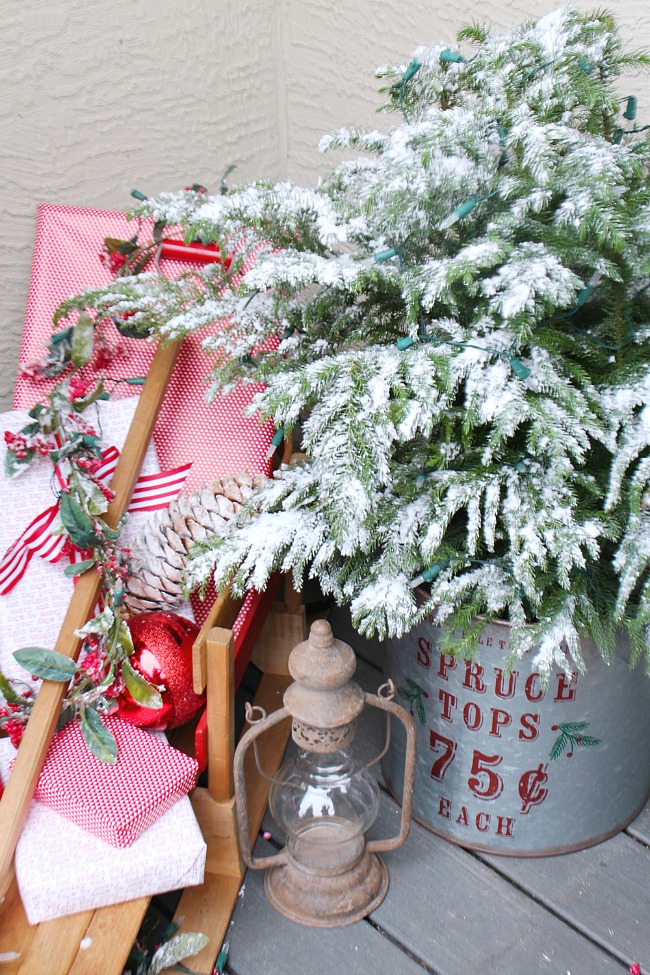 Vintage inspired Christmas front porch with sleds, flocked trees, and red and white presents.
