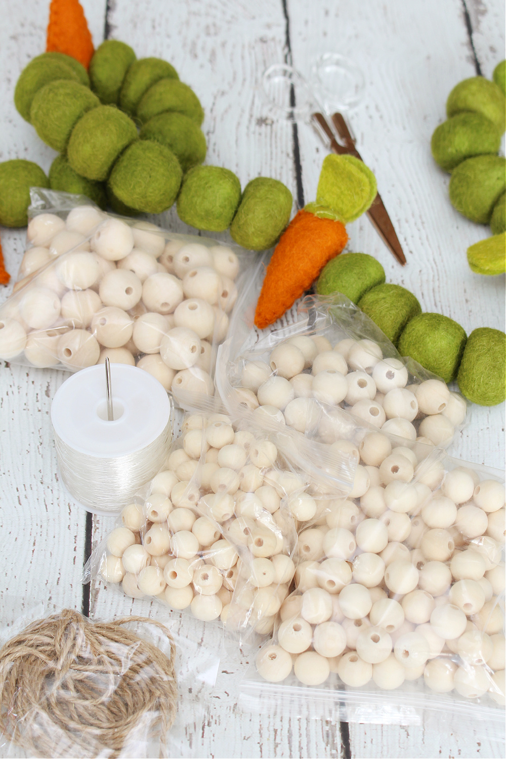 Materials for a DIY felted carrot and wood bead Easter garland.